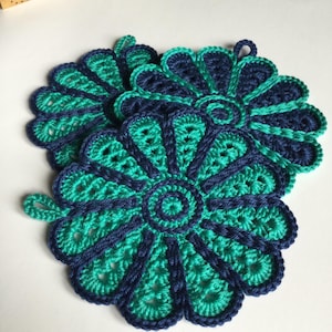 Peut inclure: Deux dessous-de-plat en crochet en forme de fleur, de couleur bleu marine et turquoise. Les dessous-de-plat ont un cercle central et un bord festonné.