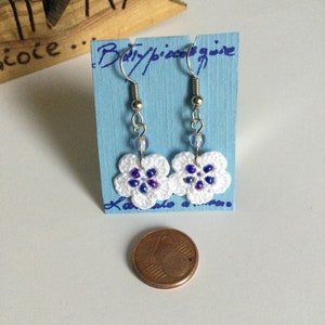 K&ouml;nnte beinhalten: Wei&szlig;e geh&auml;kelte Blumenohrringe mit blauen und violetten Perlen, die an silbernen Haken h&auml;ngen. Die Ohrringe werden auf einer blauen Karte mit dem Text "Baby/piece/wire" pr&auml;sentiert.