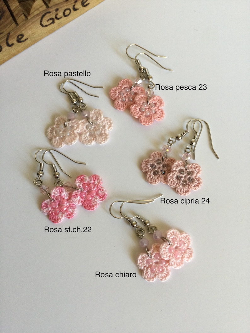 K&ouml;nnte beinhalten: Vier Paare geh&auml;kelter Blumenohrringe in verschiedenen Rosat&ouml;nen. Die Ohrringe sind mit den Farbnamen gekennzeichnet: Rosa sf.ch.22, Rosa chiaro, Rosa pesca 23 und Rosa cipria 24.