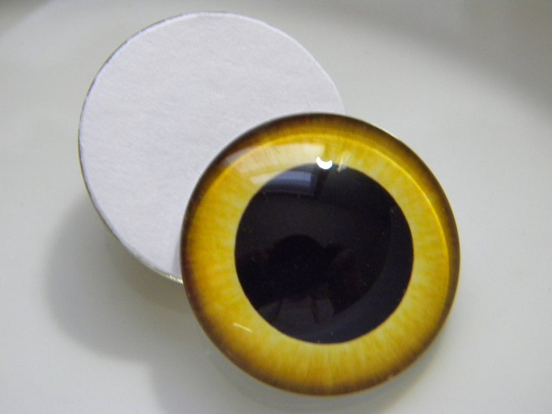 May include: A pair of yellow and brown glass eyes with black pupils. The eyes are round and have a glossy finish. They are designed for use in crafts and doll making.
