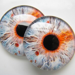 Może przedstawiać: Dwa realistyczne szklane oczy z niebieską, białą i pomarańczową tęczówką i czarną źrenicą.