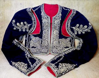 May include: A navy blue jacket with detailed silver embroidery and red lining. The jacket has floral patterns and decorative trim on the edges and sleeves. A vintage garment with a formal style.