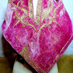 Pu&ograve; includere: Una vivace cappa di velluto rosa con ricami dorati intricati. La cappa presenta uno scollo a V ed &egrave; adornata da motivi dorati ornati. Il tessuto ha un aspetto morbido e strutturato, e il ricamo aggiunge un tocco di eleganza.