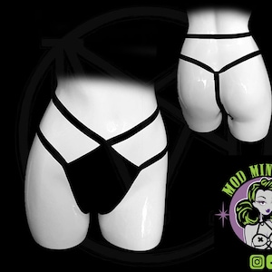 May include: Black underwear with a strappy design, displayed on a white mannequin. The design features a black panel in the front and black straps. A second view of the underwear is shown from the back. The logo for Mod Ministry is in the bottom right corner.