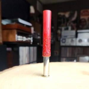May include: A red wooden bottle stopper with a silver metal base. The stopper has a textured surface and is designed to fit a standard wine bottle.