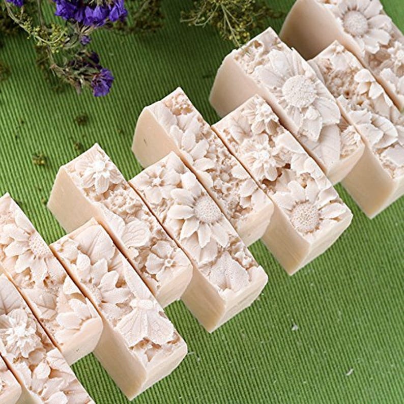 Pu&ograve; includere: Un set di otto saponette rettangolari con un design floreale. Il sapone &egrave; di colore beige chiaro e presenta un design in rilievo di fiori e foglie. Il sapone &egrave; disposto in fila su una superficie verde.