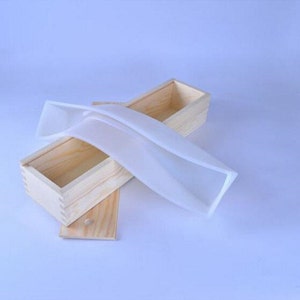 Puede incluir: Un molde de jabón de silicona blanco dentro de una caja de madera. El molde tiene forma de rectángulo con bordes redondeados. La caja es de madera clara y tiene una tapa.