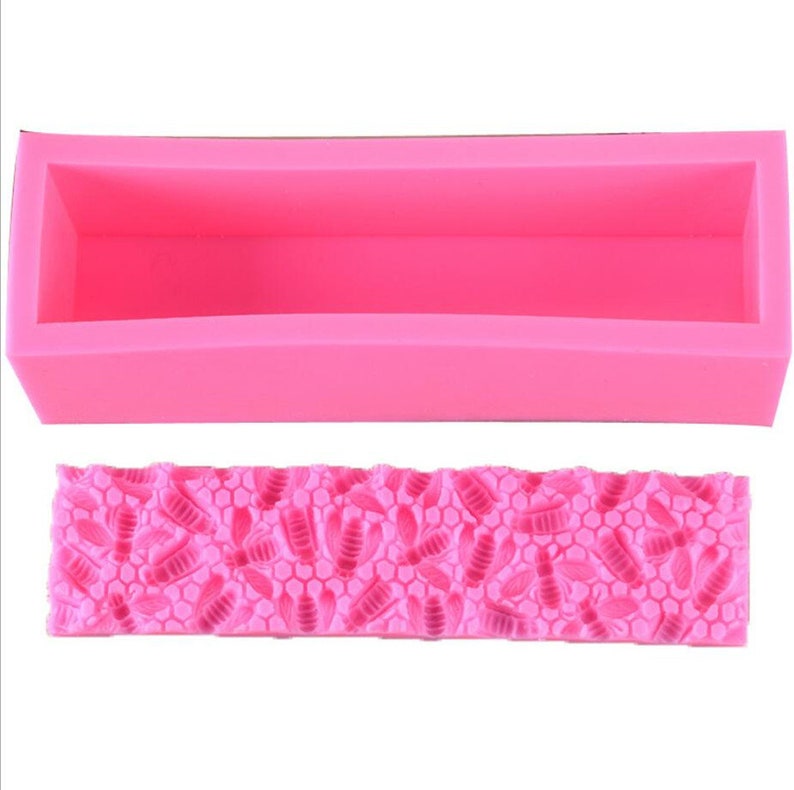 May include: A bright pink silicone soap mold with a rectangular shape and a detailed bee and honeycomb pattern. The mold is designed for creating handmade soaps or crafts, offering a decorative element.
