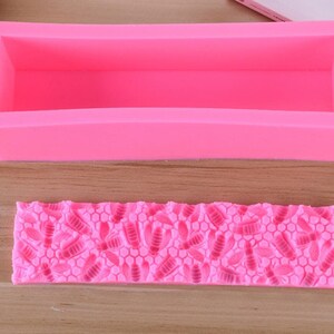May include: A bright pink silicone soap mold and a matching bee-themed soap stamp. The rectangular mold is designed for creating bar soaps. The stamp features a honeycomb pattern with bee and leaf details, perfect for adding decorative elements to handmade soaps.