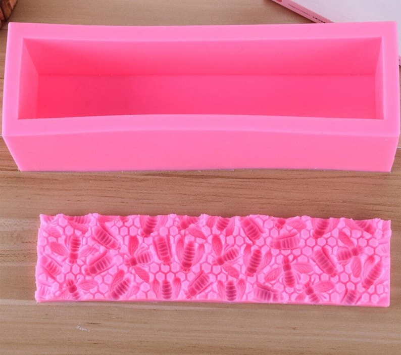 May include: A bright pink silicone soap mold and a matching bee-themed soap stamp. The rectangular mold is designed for creating bar soaps. The stamp features a honeycomb pattern with bee and leaf details, perfect for adding decorative elements to handmade soaps.