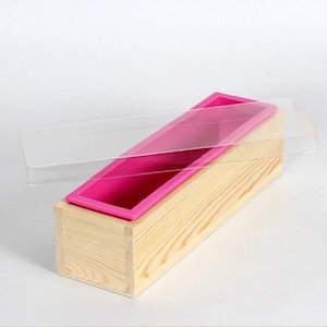 May include: A wooden box with a clear lid and a pink silicone mold inside. The mold is for making soap.