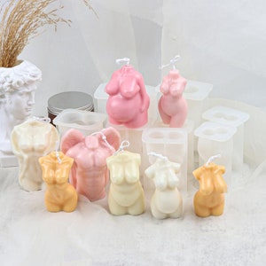 May include: Assortment of silicone molds for making candles in the shape of human figures. The molds are white and are arranged on a white surface. There are several finished candles in the molds, including pink, beige, and orange.