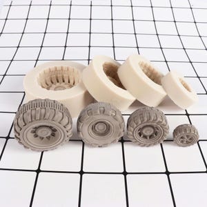 Può includere: Set di sei stampi in silicone per realizzare decorazioni per torte a forma di pneumatici di diverse dimensioni. Gli stampi sono bianchi e gli pneumatici sono grigi.
