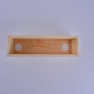 Pu&ograve; includere: Una scatola di legno con due fori circolari tagliati nella parte superiore. La scatola &egrave; realizzata in legno chiaro e ha una finitura naturale.