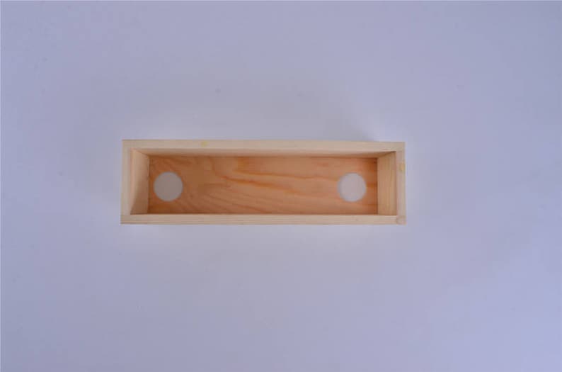 Pu&ograve; includere: Una scatola di legno con due fori circolari tagliati nella parte superiore. La scatola &egrave; realizzata in legno chiaro e ha una finitura naturale.