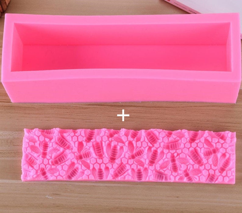 May include: A bright pink silicone soap mold set. The top mold is a rectangular box. The bottom mold has a bee and honeycomb pattern. The molds are designed for crafting homemade soaps.