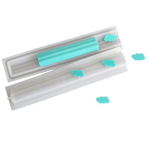 May include: A silicone mold for making candy or polymer clay. The mold is shaped like a long rectangle with a groove down the center. There are four small cloud-shaped pieces of candy or clay next to the mold.