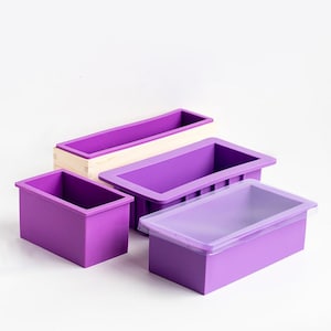 Op de afbeelding: Vier paarse siliconen zeepvormen, waaronder een met een houten basis en een met een doorzichtig deksel.