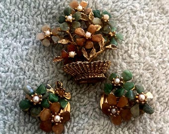 May include: A gold-tone jewelry set consisting of a brooch and two matching clip-on earrings. Each piece features a floral arrangement with green and amber-colored stone petals, gold-tone metal leaves, and small white faux pearl centers.