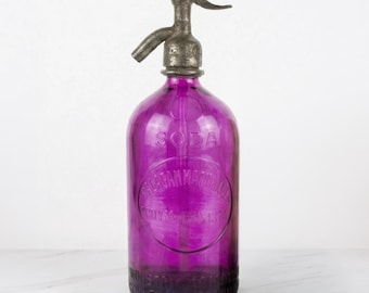 May include: A vintage purple glass soda siphon bottle featuring a metallic silver-toned spout and handle. The glass body is embossed with the text SODA and a circular emblem containing the words BALAGAN MARCONI and the year 1874.