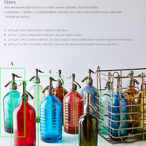 May include: A collection of vintage-style glass seltzer bottles with metal siphon tops in various colours including red, blue, green, and amber. Some bottles feature ribbed glass textures and engraved text, displayed individually and within a wire crate.