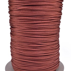 May include: A spool of copper-colored cord. The cord is tightly wound around a cardboard core. The cord appears to be made of a smooth, woven material. The spool is sitting on a white background.
