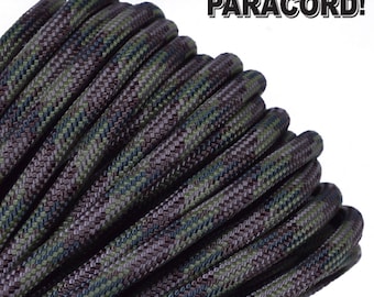 Puede incluir: Primer plano de una bobina de paracord de camuflaje verde, marrón y negro. El paracord está enrollado apretado y tiene una superficie texturizada.
