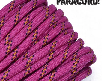 Puede incluir: Primer plano de un paracord rosa con rayas negras y doradas. El paracord está enrollado y listo para ser utilizado para manualidades.
