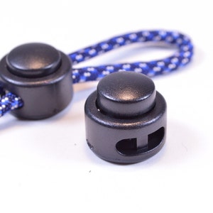 May include: Two black plastic cord locks with a blue and white patterned cord. The cord locks have a round button on one side and a slot on the other side for securing the cord.