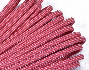 Puede incluir: Primer plano de un haz de cordones trenzados rojos y blancos. Los cordones están tejidos con un patrón repetitivo de hilos rojos y blancos. Los cordones probablemente se utilizan para manualidades u otros proyectos de bricolaje.