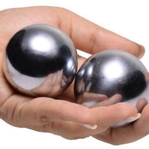 Op de afbeelding: Twee zilveren metalen ballen, ook wel Baoding-ballen genoemd, worden in de hand van een persoon gehouden. De ballen zijn glad en glanzend.