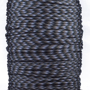 May include: A spool of camouflage paracord with a black, brown, and white pattern. The paracord is wound tightly around a cardboard spool.