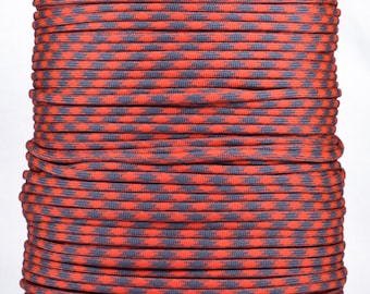 May include: A spool of red and gray paracord with a diamond pattern. The paracord is wound tightly around the spool.