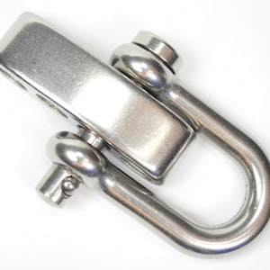 May include: A stainless steel D-shackle with a rectangular top and a curved, U-shaped bottom. The shackle has a polished, metallic finish and is designed for heavy-duty use. The shackle is shown against a white background.