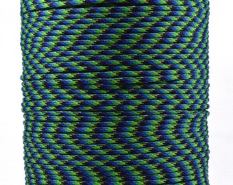 May include: A spool of multi-colored paracord. The cord features a repeating pattern of black, green, and blue. The spool is cylindrical and sits on a gray cardboard base. The cord is tightly wound, creating a textured surface.