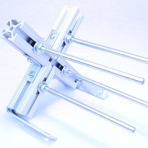 Może przedstawiać: Srebrny metalowy wspornik z czterema srebrnymi metalowymi prętami przymocowanymi do niego. Wspornik jest wykonany z aluminium i ma srebrne wykończenie. Pręty są przymocowane do wspornika za pomocą śrub i nakrętek.