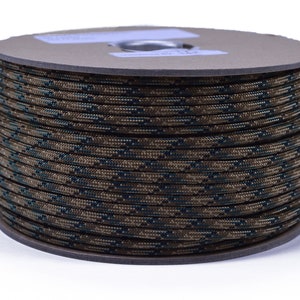 May include: A spool of camouflage paracord, a type of strong nylon rope, in a brown and green color pattern. The paracord is wound tightly around a cardboard spool.