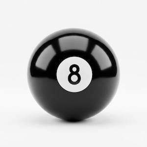 May include: A glossy black billiard ball featuring a white circular inlay on the front. Centered within the white circle is the black numeral eight. The surface of the sphere is smooth and reflective, showing light highlights across the top curve.