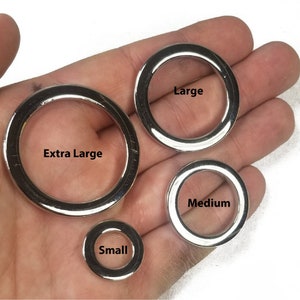 K&ouml;nnte beinhalten: Vier silberne Metallringe in verschiedenen Gr&ouml;&szlig;en. Die Ringe sind mit "Klein", "Mittel", "Gro&szlig;" und "Extra Gro&szlig;" beschriftet.