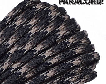Puede incluir: Primer plano de un paracord negro y marrón con un patrón de camuflaje. El paracord está enrollado y listo para ser usado para manualidades o supervivencia.