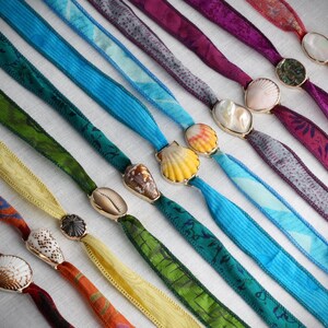May include: An assortment of colorful ribbon lanyards with seashell pendants. The ribbons vary in color, including red, green, yellow, and blue, and feature various patterns. The pendants are made of seashells and are attached to the ribbons with gold-colored metal.
