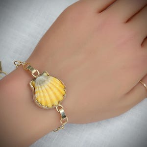 May include: A gold chain bracelet with a yellow and white seashell charm.