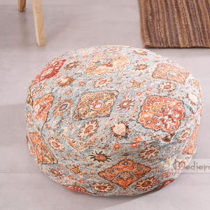 Könnte beinhalten: Ein runder Hocker mit einem Muster in Blau, Orange und Rot. Der Stoff hat ein detailliertes, blumenähnliches Muster. Dieses niedrige, gepolsterte Möbelstück eignet sich zum Sitzen oder als Fußstütze. Der Stil ist böhmisch oder Vintage, mit einem weichen, einladenden Aussehen.