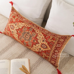 May include: A long rectangular throw pillow with a red, cream, and blue patterned design. The pillow has tassels on each end.