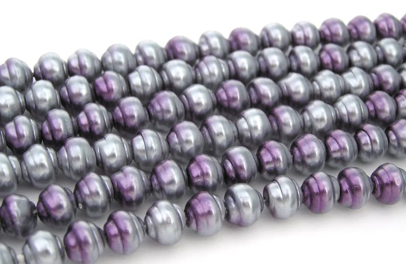 May include: A strand of purple and silver iridescent glass beads. The beads are oval shaped and have a smooth, glossy finish.