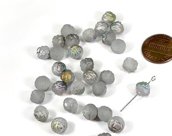 May include: A collection of iridescent gray glass beads with a rose design. The beads are scattered on a white surface next to a US penny.
