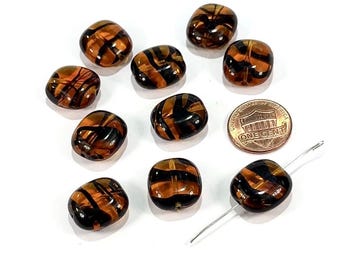 May include: A collection of ten brown and black glass beads with a striped design. A US penny is included for size comparison. The beads are irregularly shaped and have a glossy finish. A needle is also included.