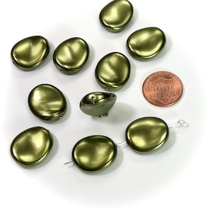 May include: Olive green, oval-shaped beads with a metallic sheen are scattered on a white surface. A U.S. one-cent coin is included for size reference. The beads have a smooth, slightly irregular surface and are designed for jewelry making.