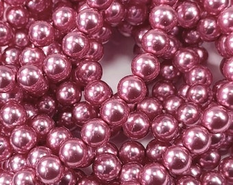 May include: Close-up of a pile of mauve-colored, round beads. The beads have a glossy, reflective surface, suggesting a pearl-like finish. The beads are clustered together, creating a dense, textured appearance. Ideal for jewelry making and crafts.