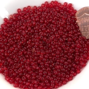 Könnte beinhalten: Ein großer Haufen kleiner, runder, roter Glasperlen. Die Perlen sind durchscheinend und haben einen leichten Glanz. Die Perlen sind in einem zufälligen Muster angeordnet.